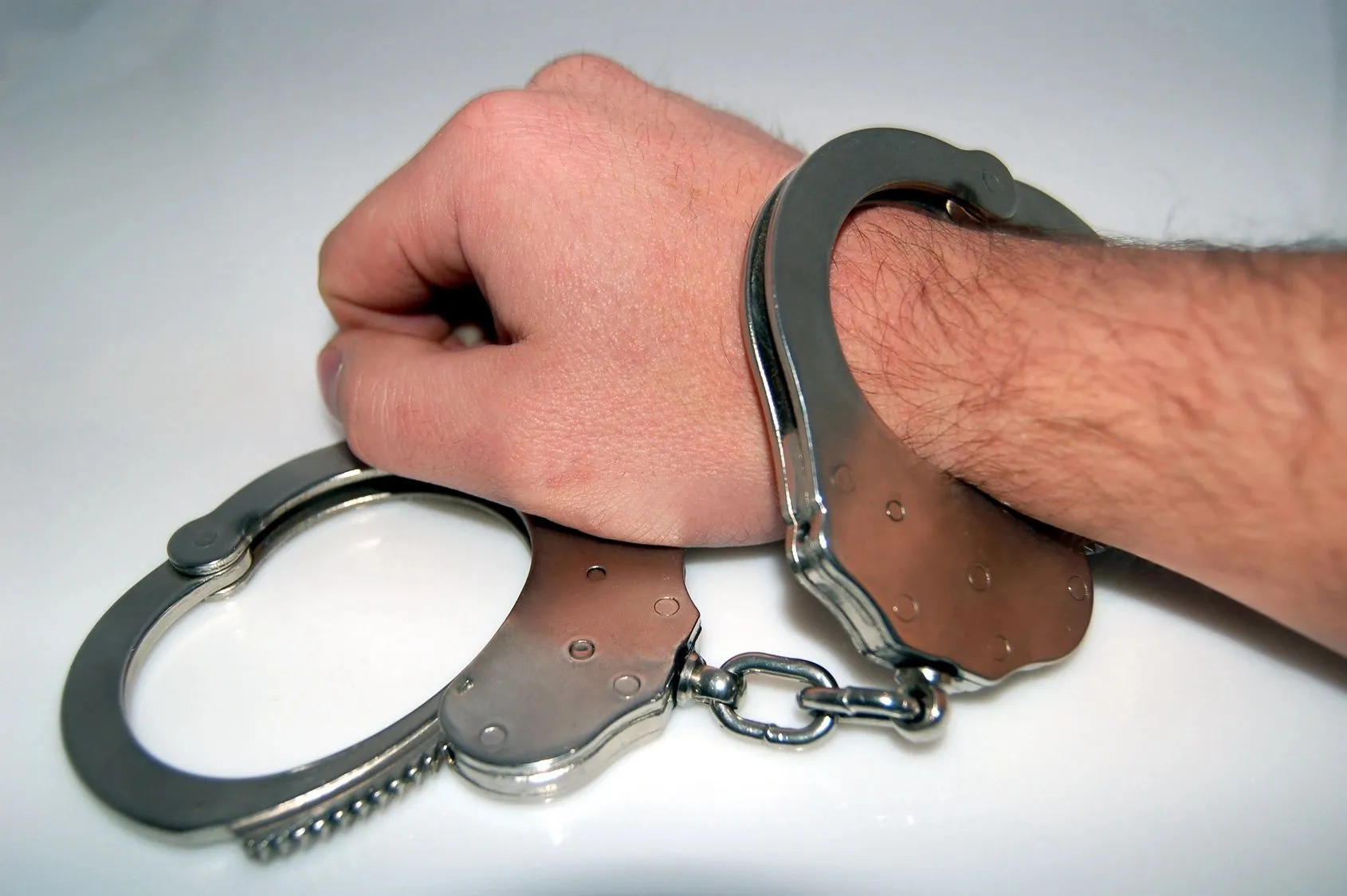 A man 's hand is holding on to some handcuffs.