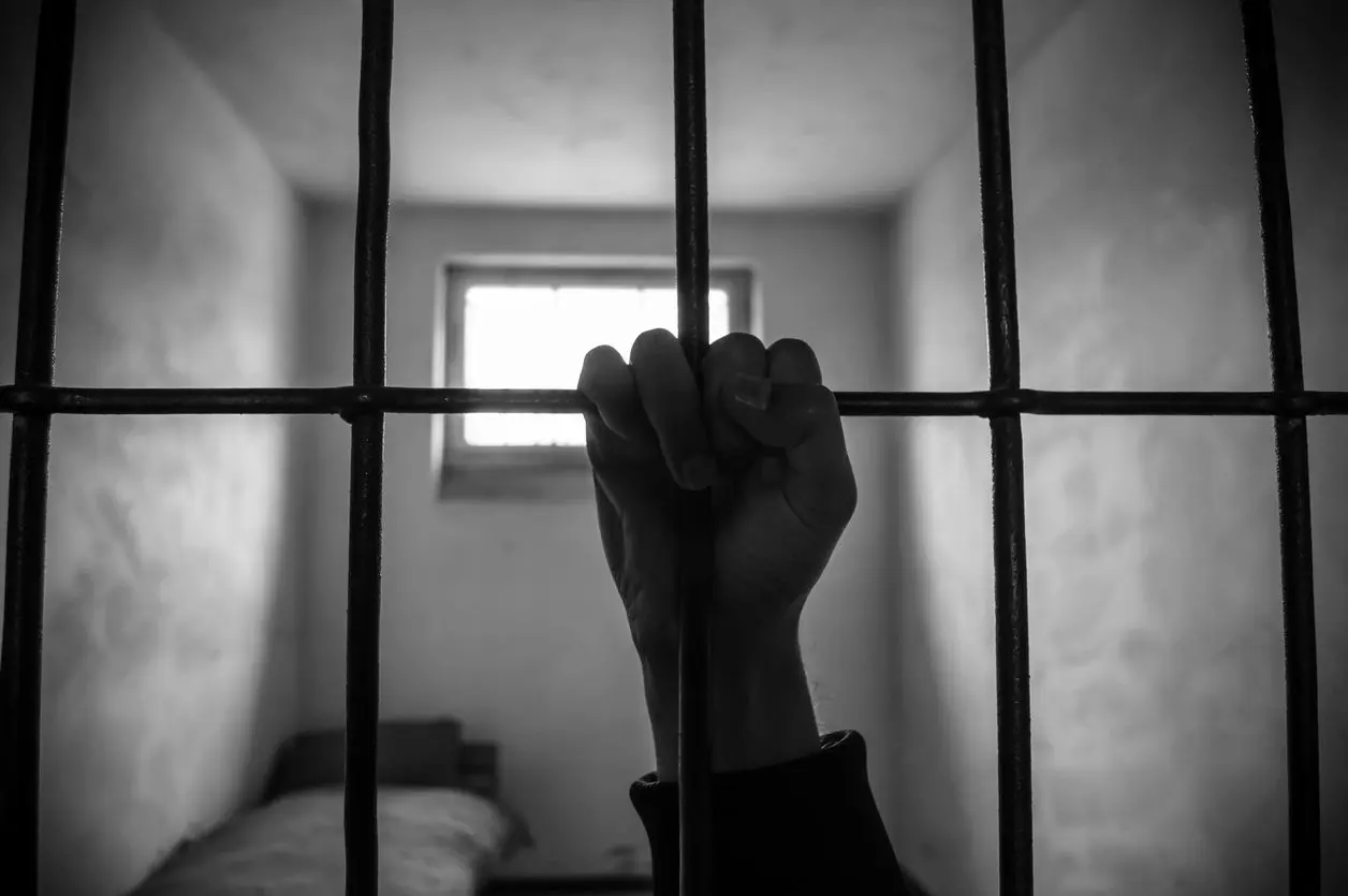 A person 's hand is holding onto bars in a jail cell.